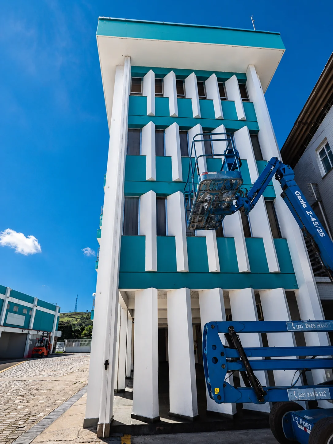 Inspeção técnica em fachada de edifício industrial com plataforma elevatória.